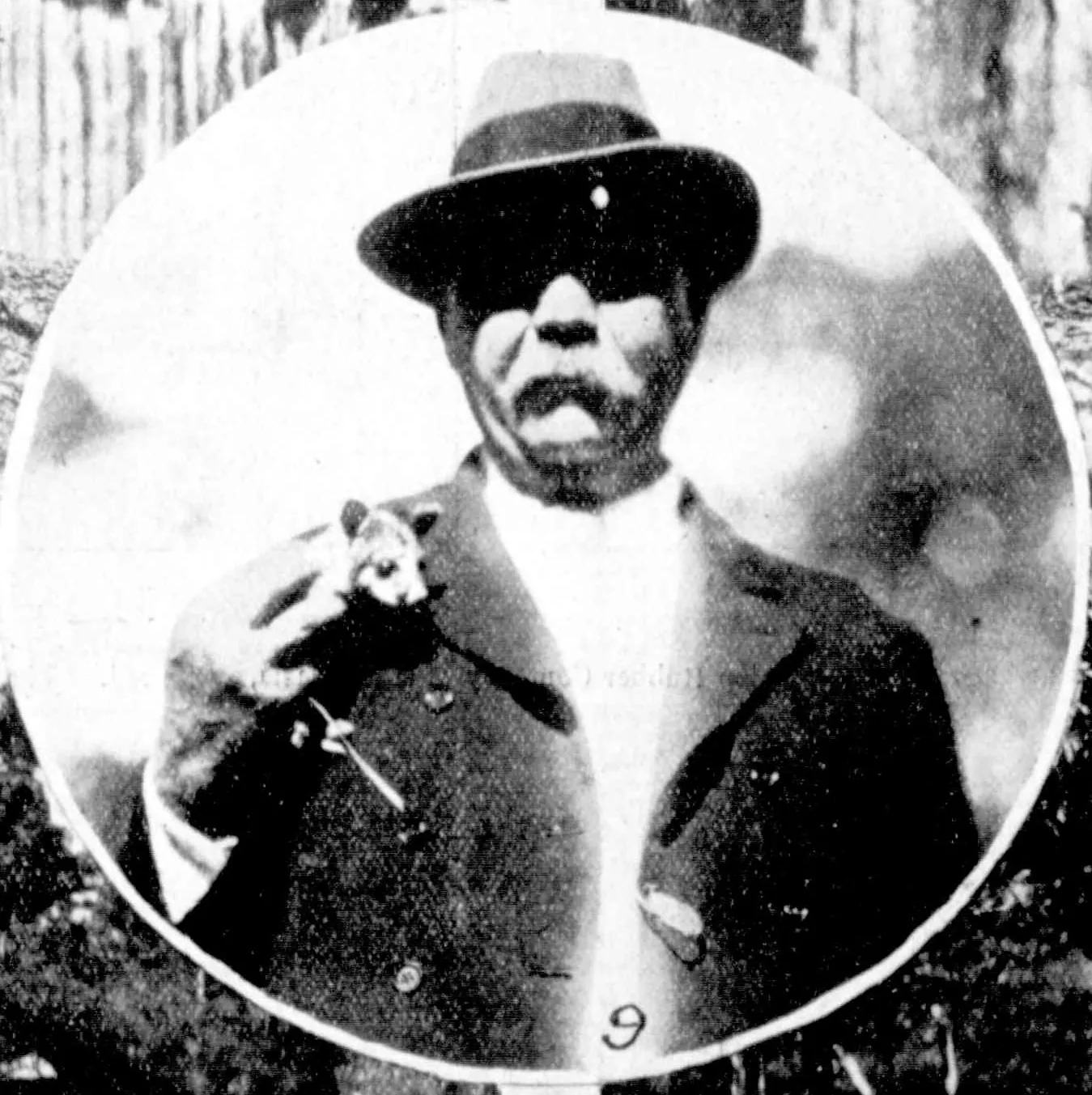 Conan Doyle in a soft felt hat and a dark coat, holding a baby possum up against his chest, in a round frame.
